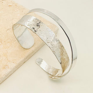 A Sterling Silver Cuff Bracelet, split with one smooth piece folded over and soldered to the other half which is finished with a textured cross peen hammer. Elegant and Stunning.